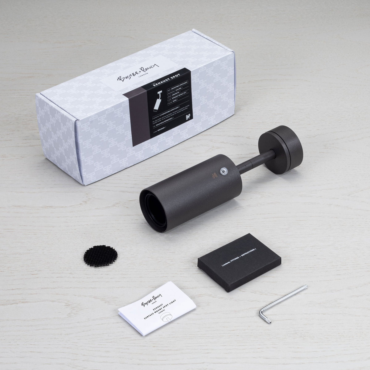 A Buster + Punch Exhaust Spot light in graphite, with its packaging, instructions, and an Allen key on a wooden surface.