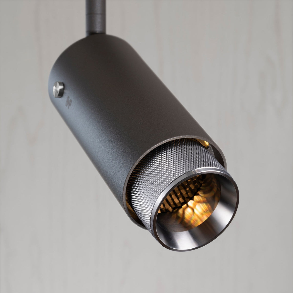 Close-up of a dark grey cylindrical track light with a textured silver interior and warm glow.