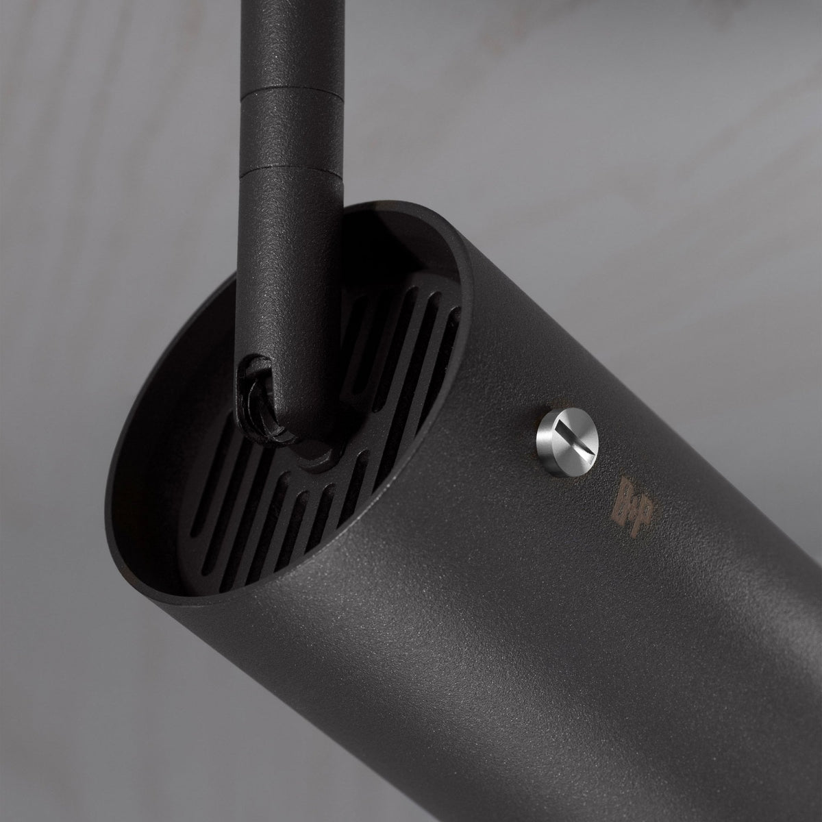 Close-up of a black cylindrical light fixture with a textured finish, a silver screw, and a subtle logo.