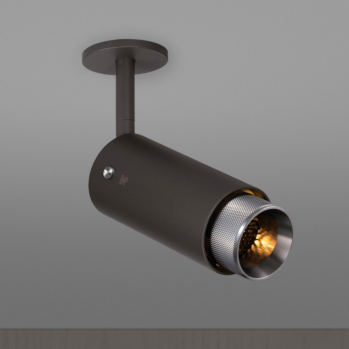 Dark grey cylindrical ceiling spotlight with a textured silver inner rim and warm glowing bulb.