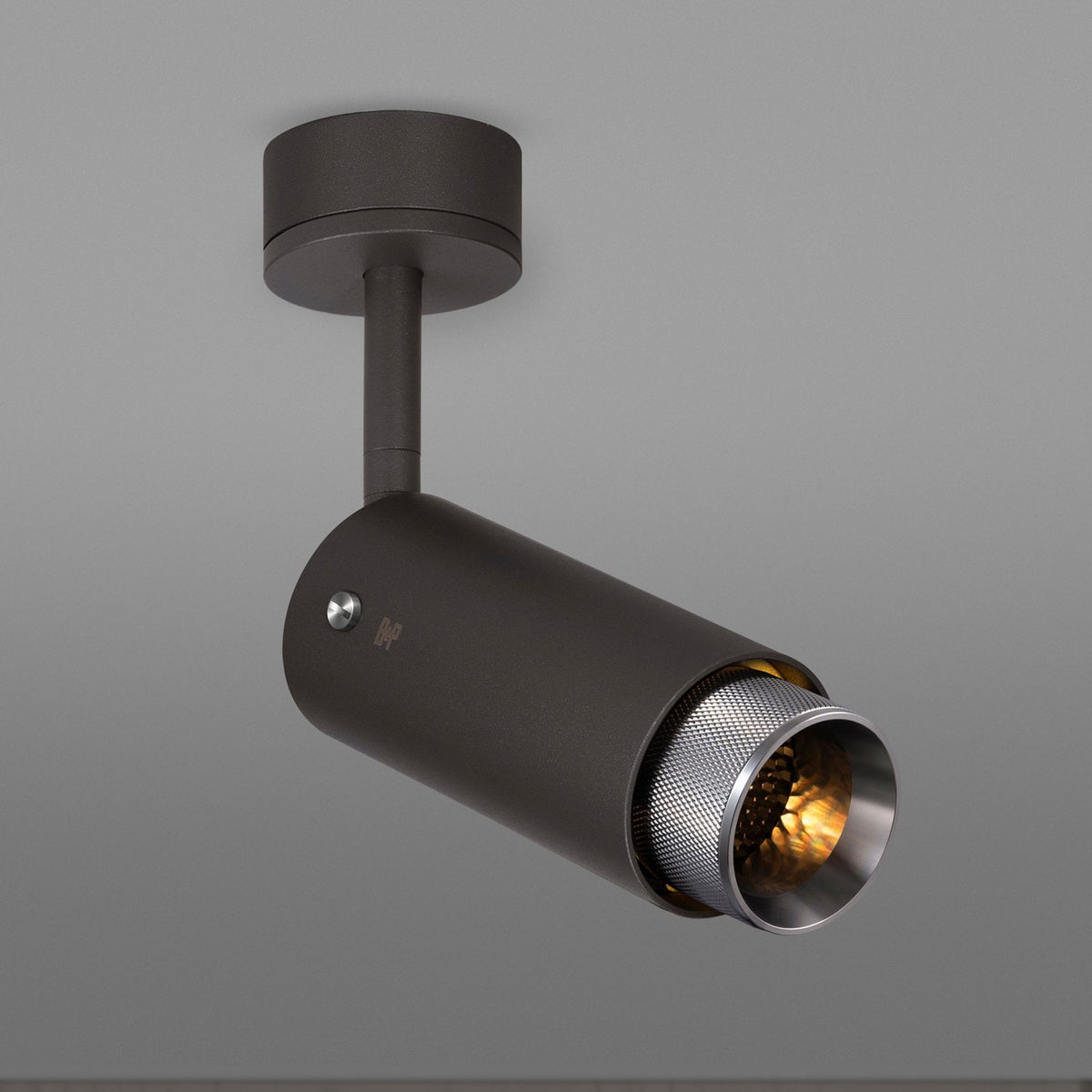 Dark grey cylindrical ceiling spotlight with a textured silver inner rim and warm light glowing from within. 