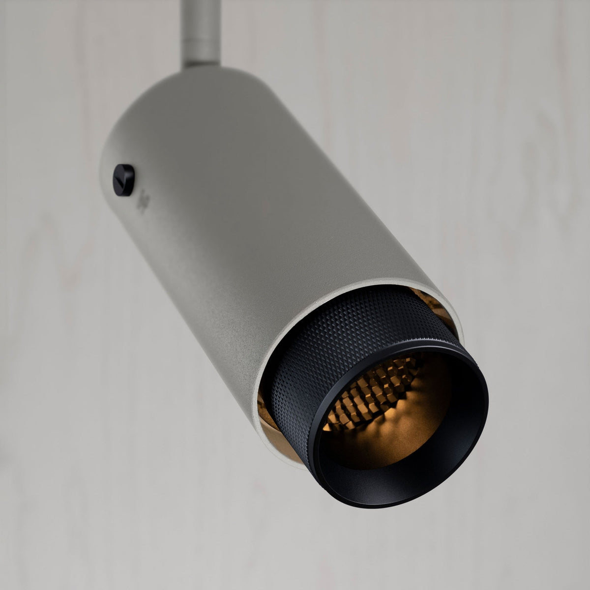 Close-up of a light grey cylindrical track light with a black textured interior and warm golden light.