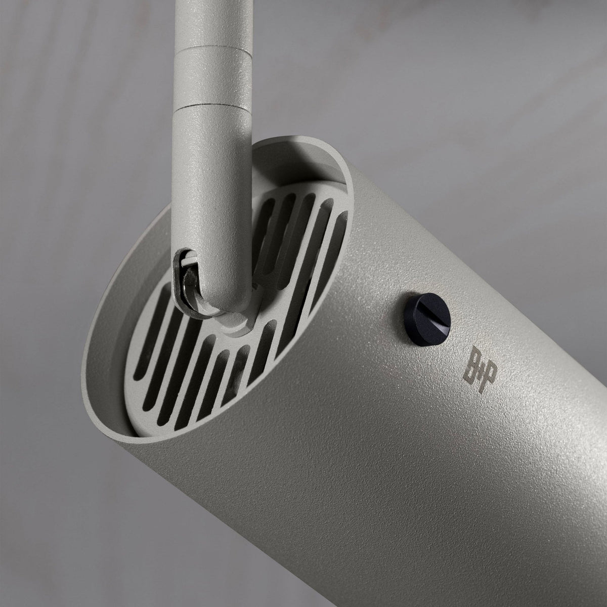 Close-up of a light grey cylindrical track light with a black adjustment knob and B+P logo.