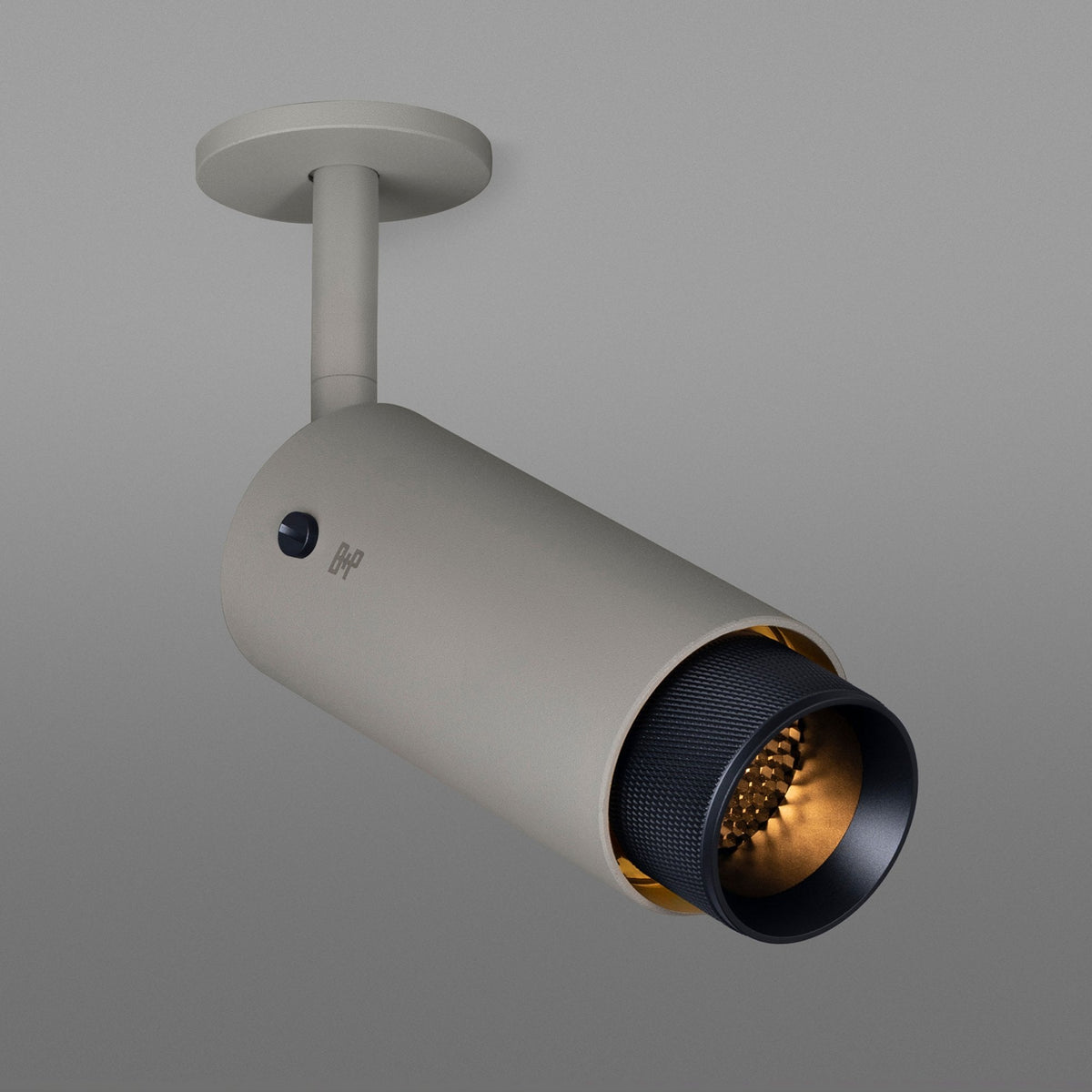 A beige cylindrical ceiling spotlight with a black textured inner rim and warm golden light.
