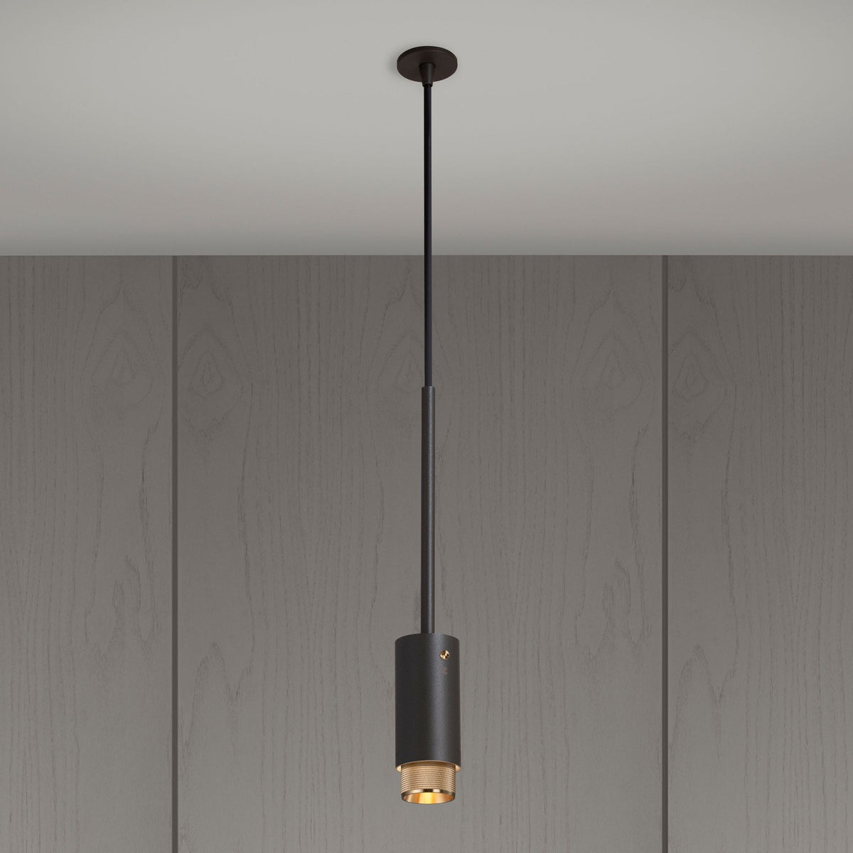 A dark grey cylindrical pendant light with a gold interior hangs from a ceiling against a wood-paneled wall.