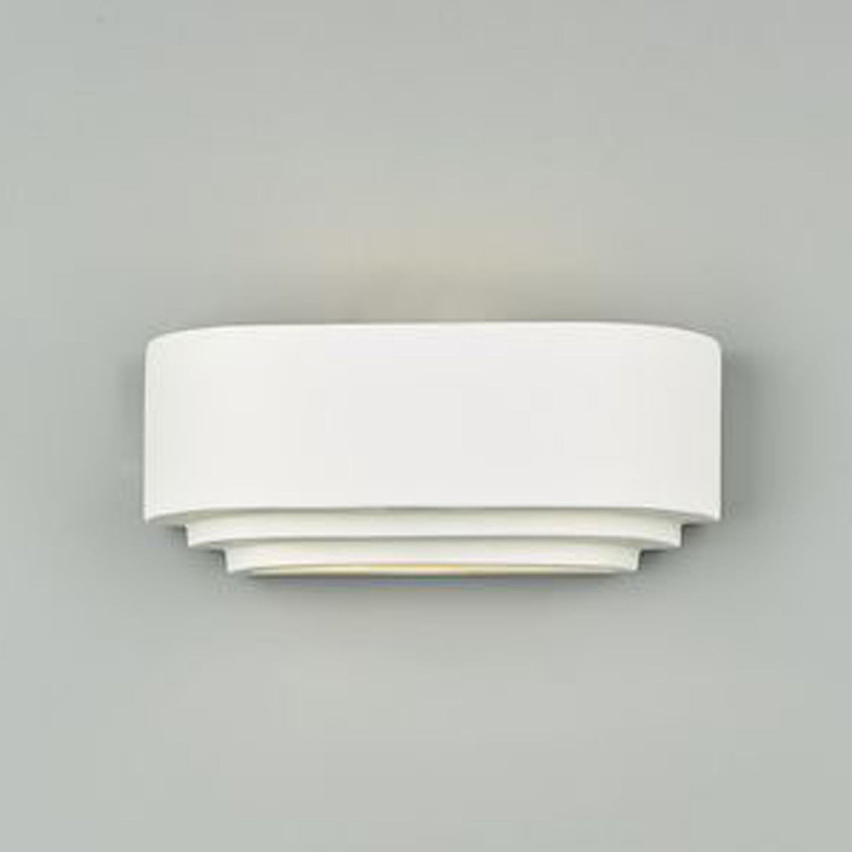 A white wall light in an oval, tiered design with light shining through the tiers.