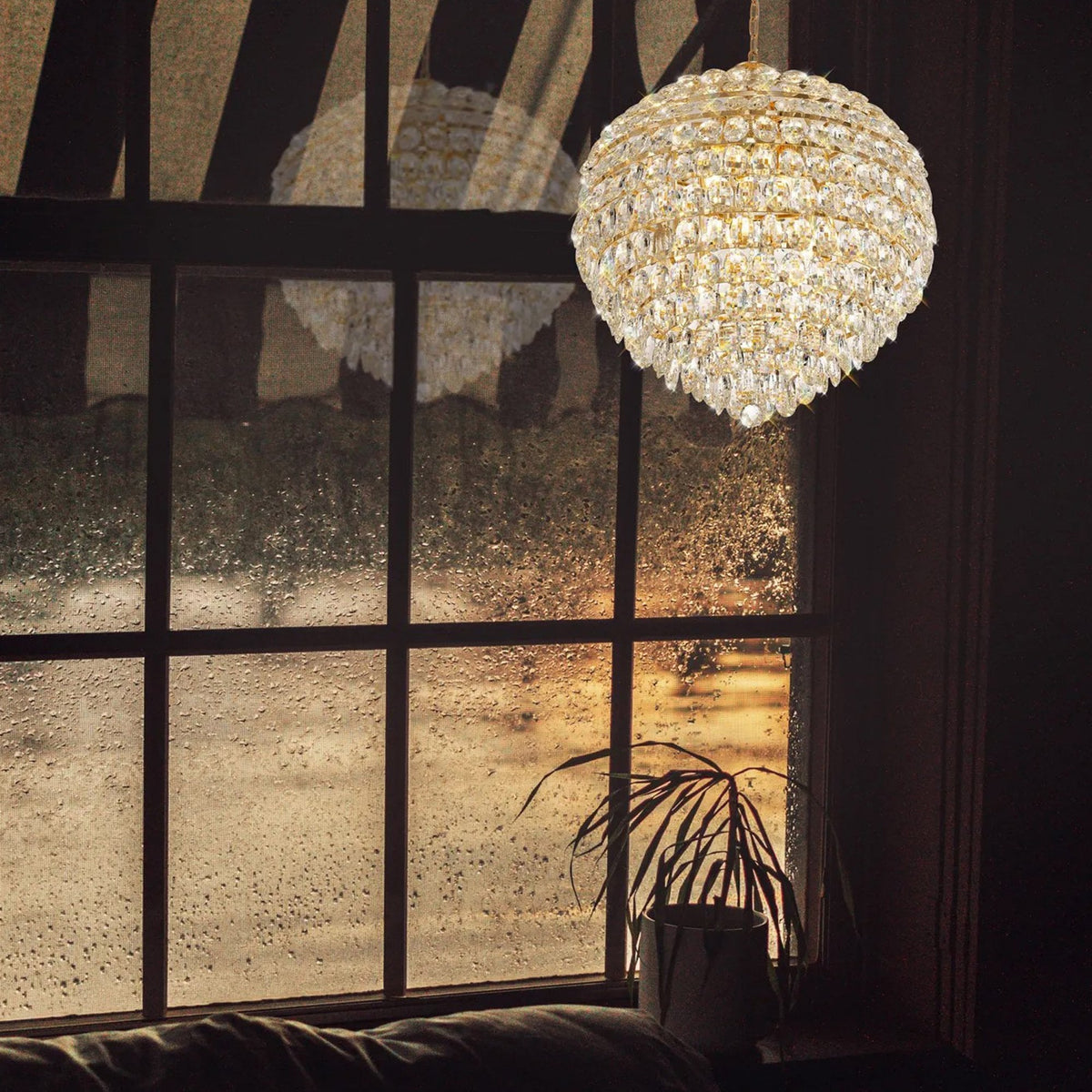 A spherical crystal chandelier illuminates a room, seen through a rain-streaked window.