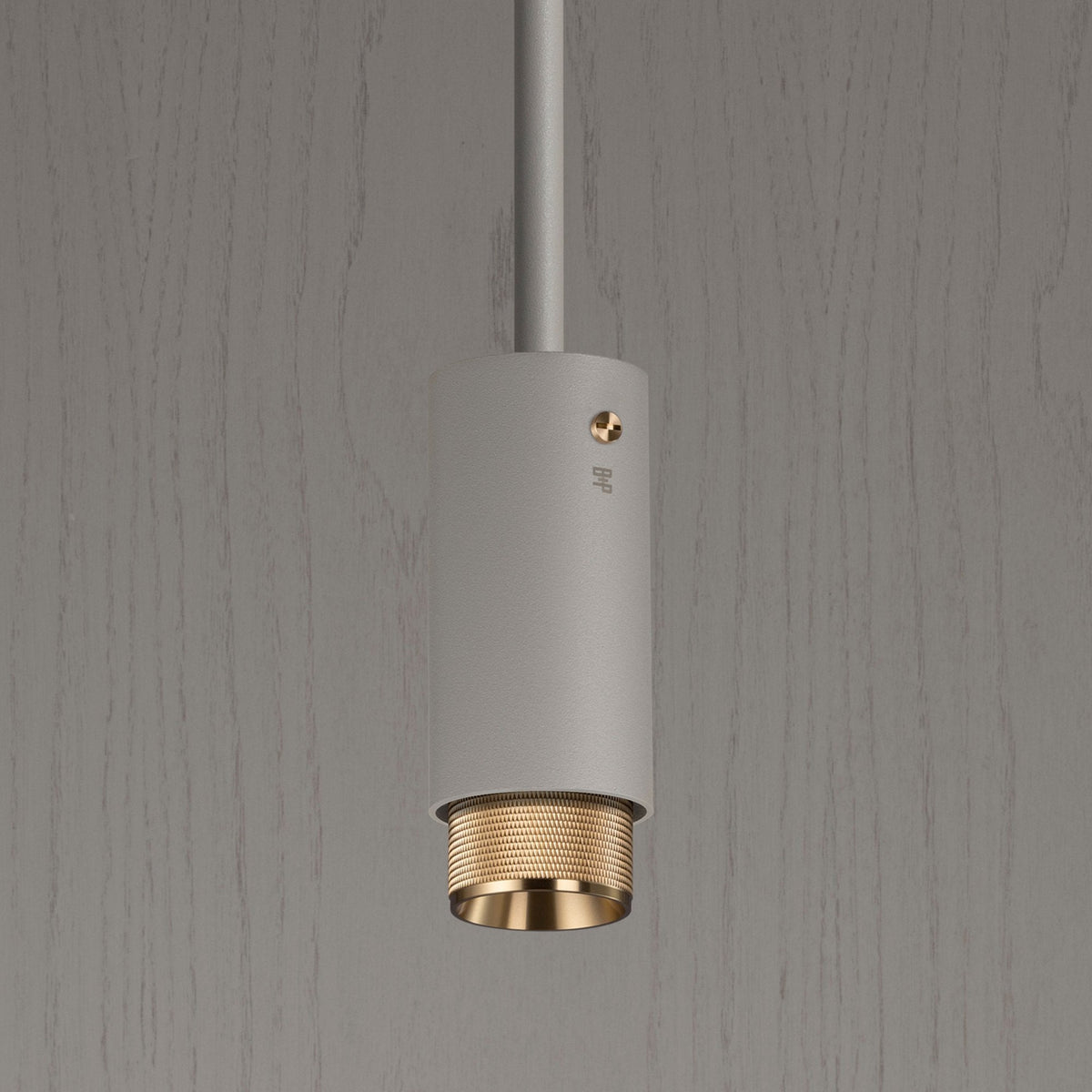A modern, cylindrical pendant light in matte white with a textured brass interior, hanging against a grey wood-grain wall.