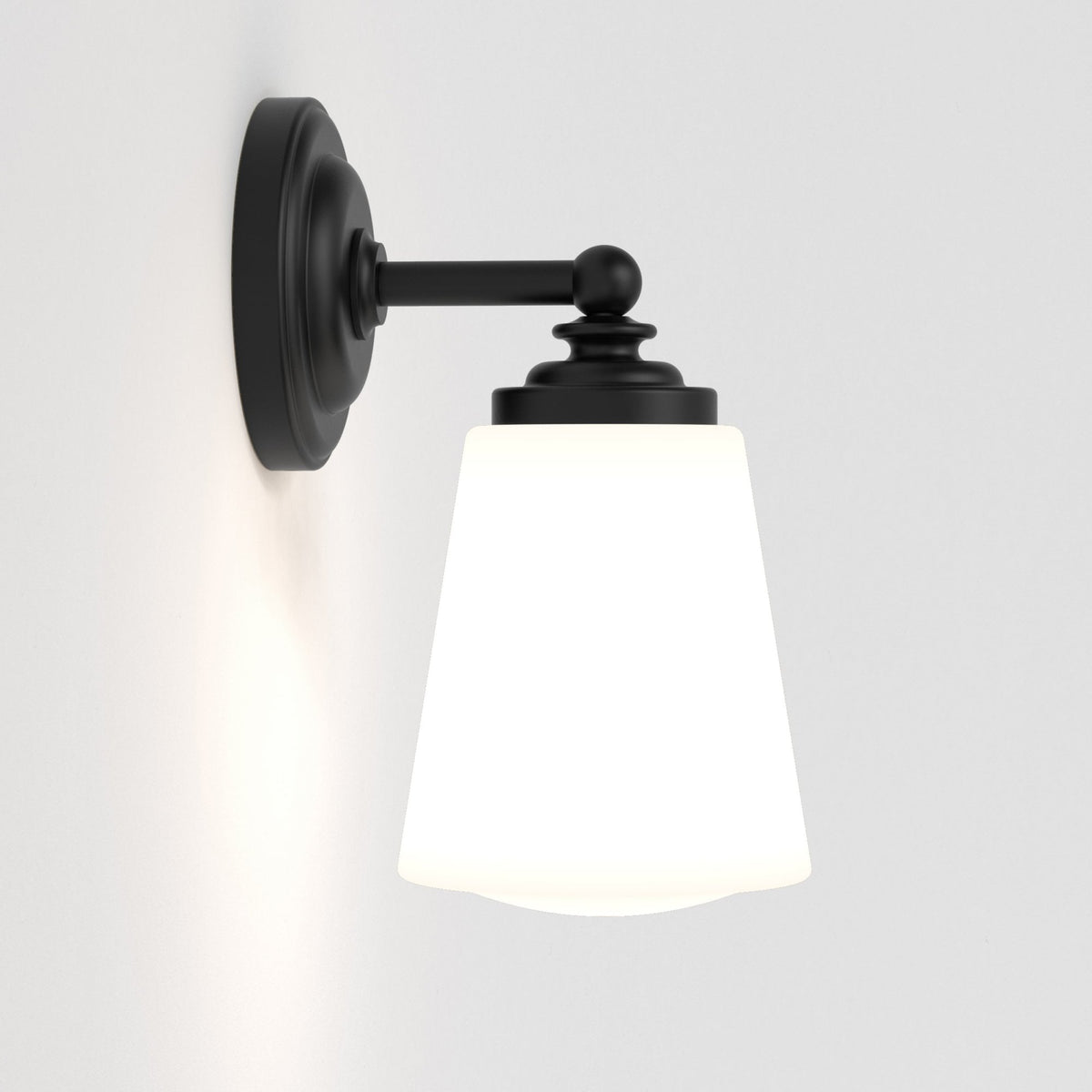 Black wall sconce with a white conical glass shade, emitting a warm glow on a white wall