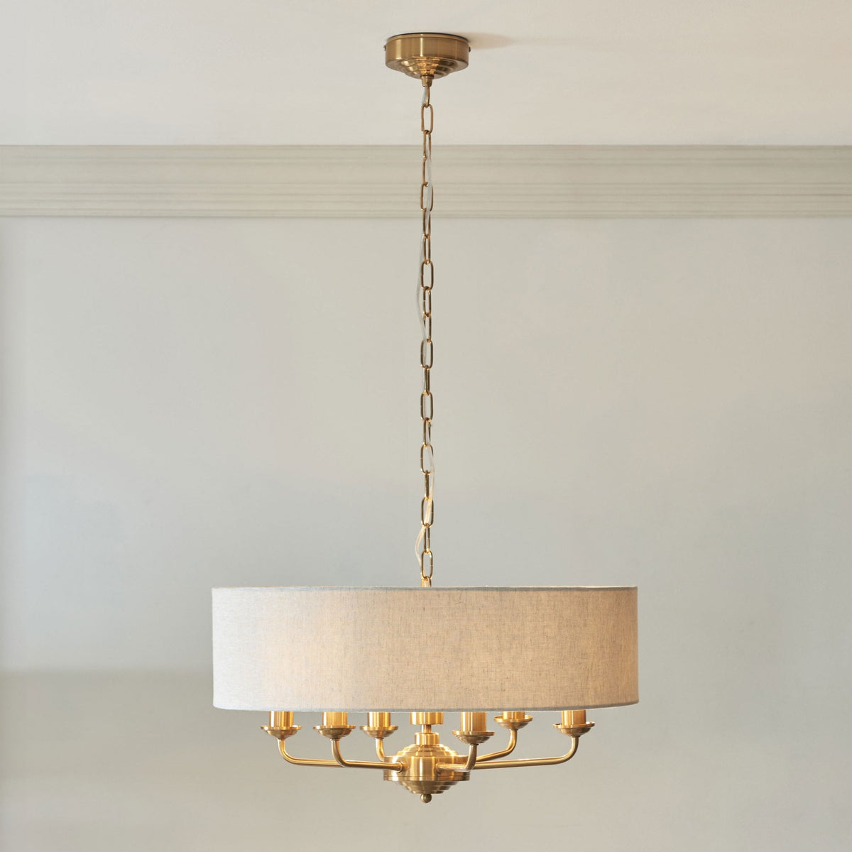 A brass chandelier with a large, round, light-colored fabric shade hangs from a ceiling.