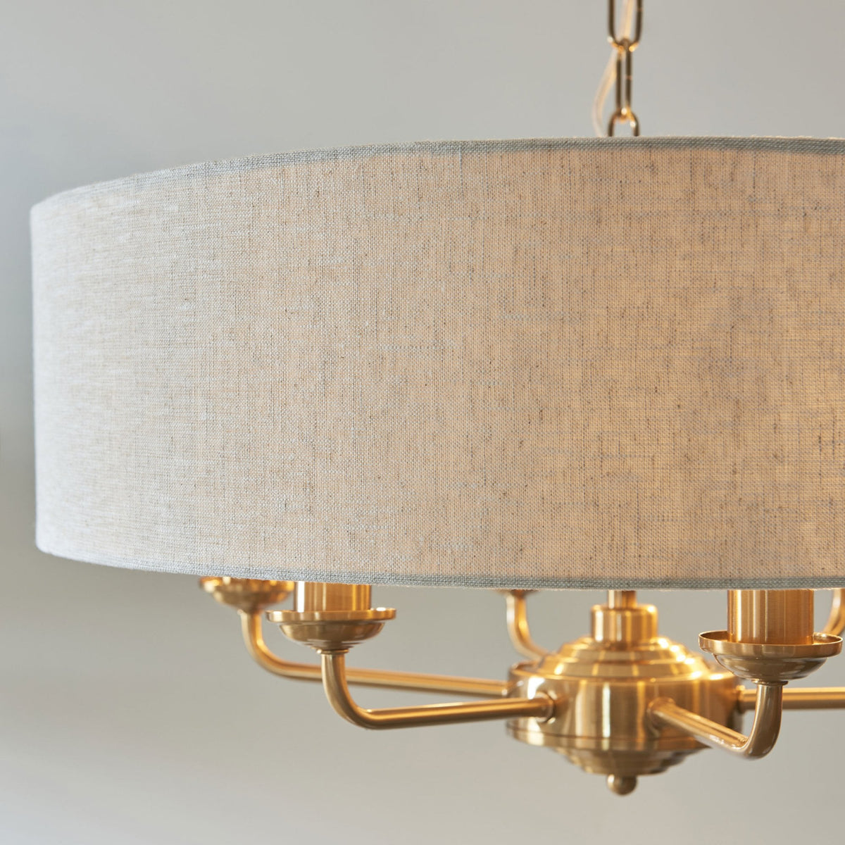 Close-up of a brass chandelier with a light-colored fabric drum shade, showing the detailed metalwork.