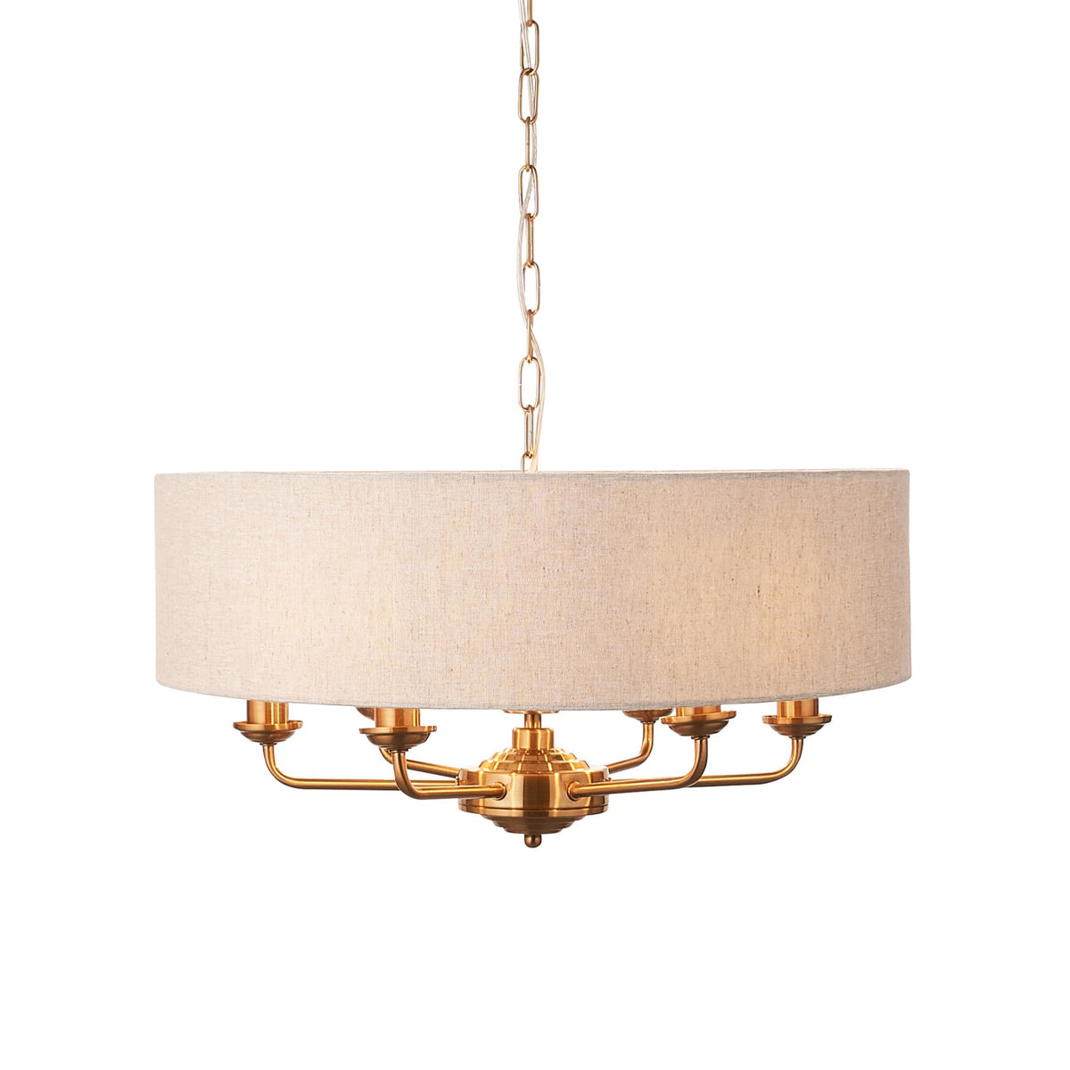 A brass chandelier with a large, round, light-colored fabric shade hangs against a white background.