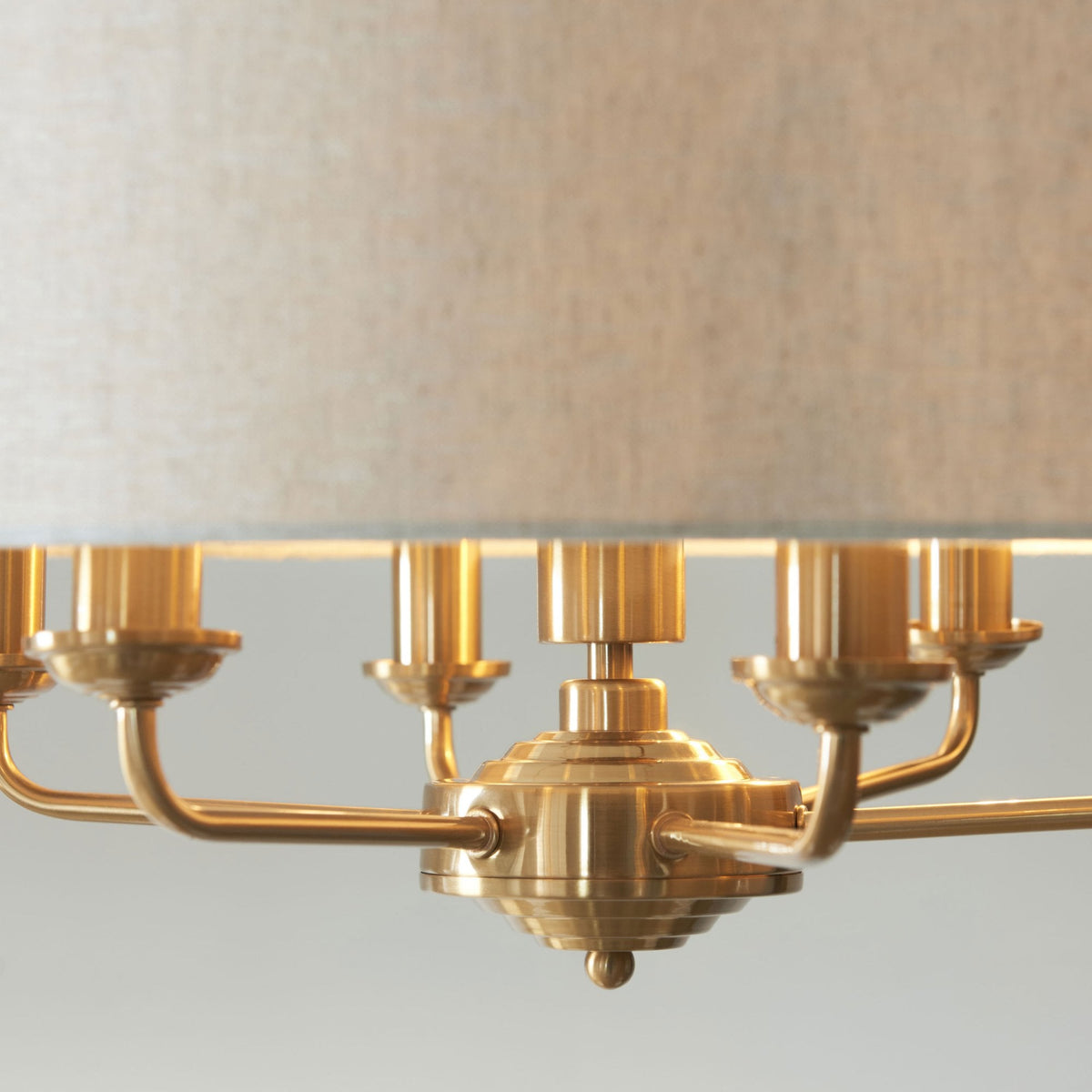 Close-up of the brass base and light-colored fabric shade of a chandelier.