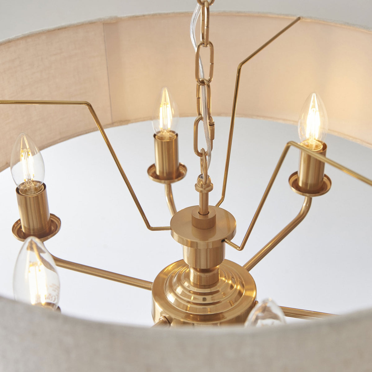 View from inside the light-colored fabric shade of a brass chandelier, showing five lit bulbs.