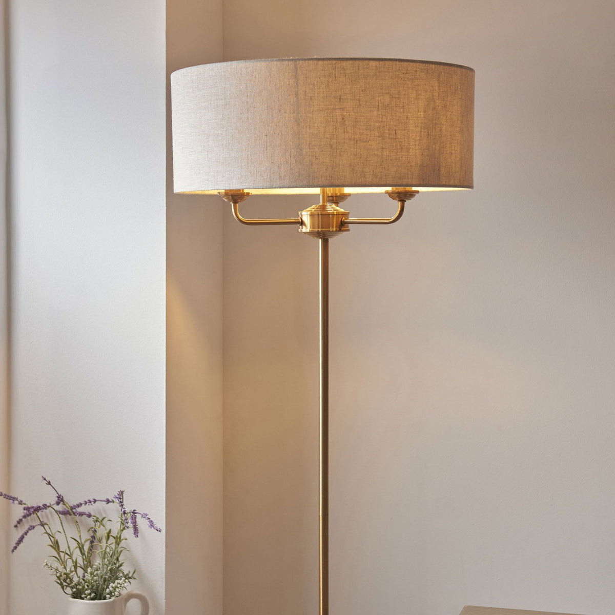 Close-up of a brass floor lamp with a cream fabric shade, casting a warm glow in a room.