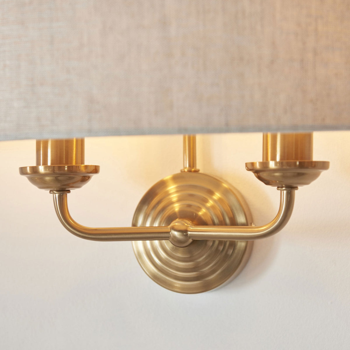 Close-up of the antique brass base of a wall light with two bulbs under a linen shade.