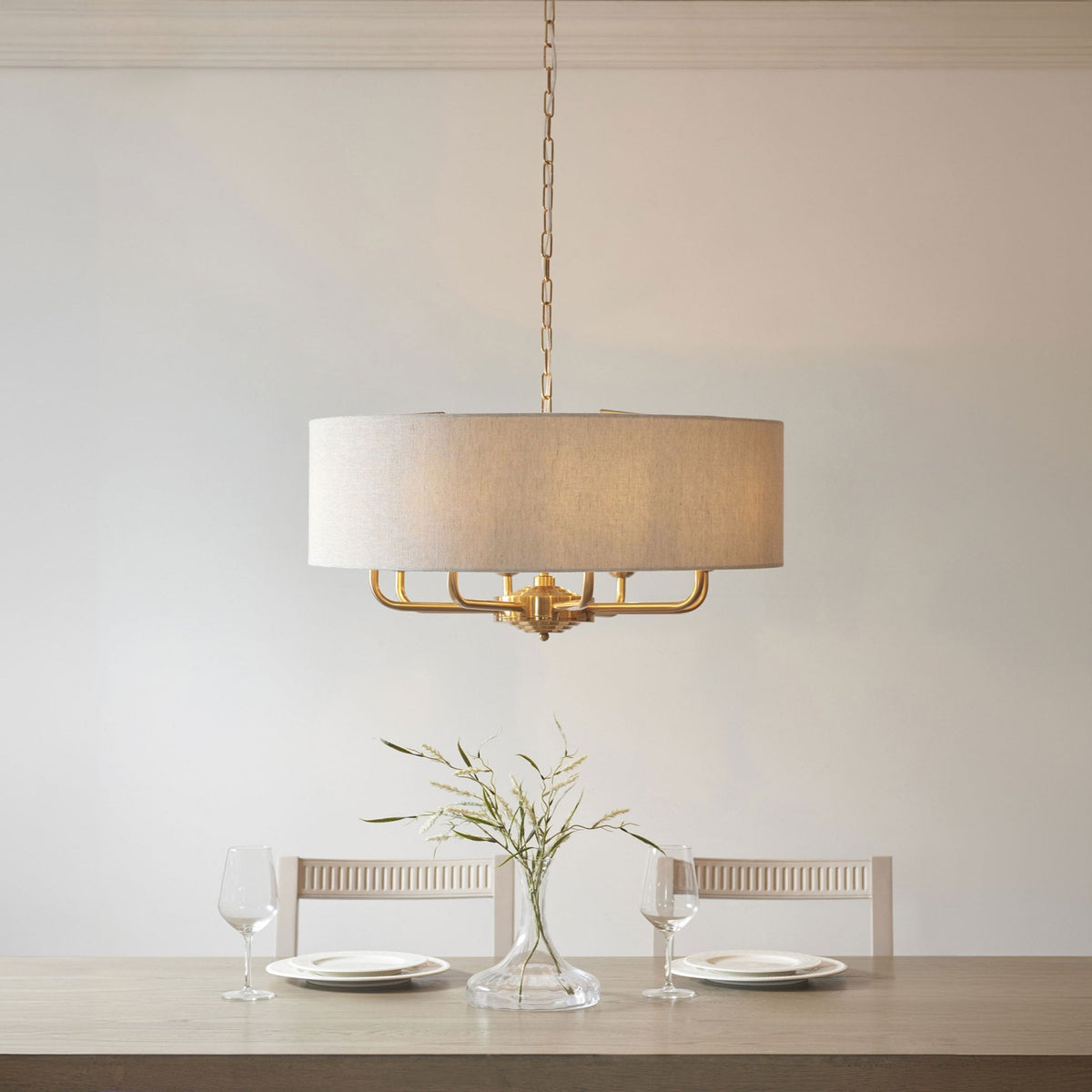 A gold chandelier with a light fabric drum shade hangs above a dining table set with two places.