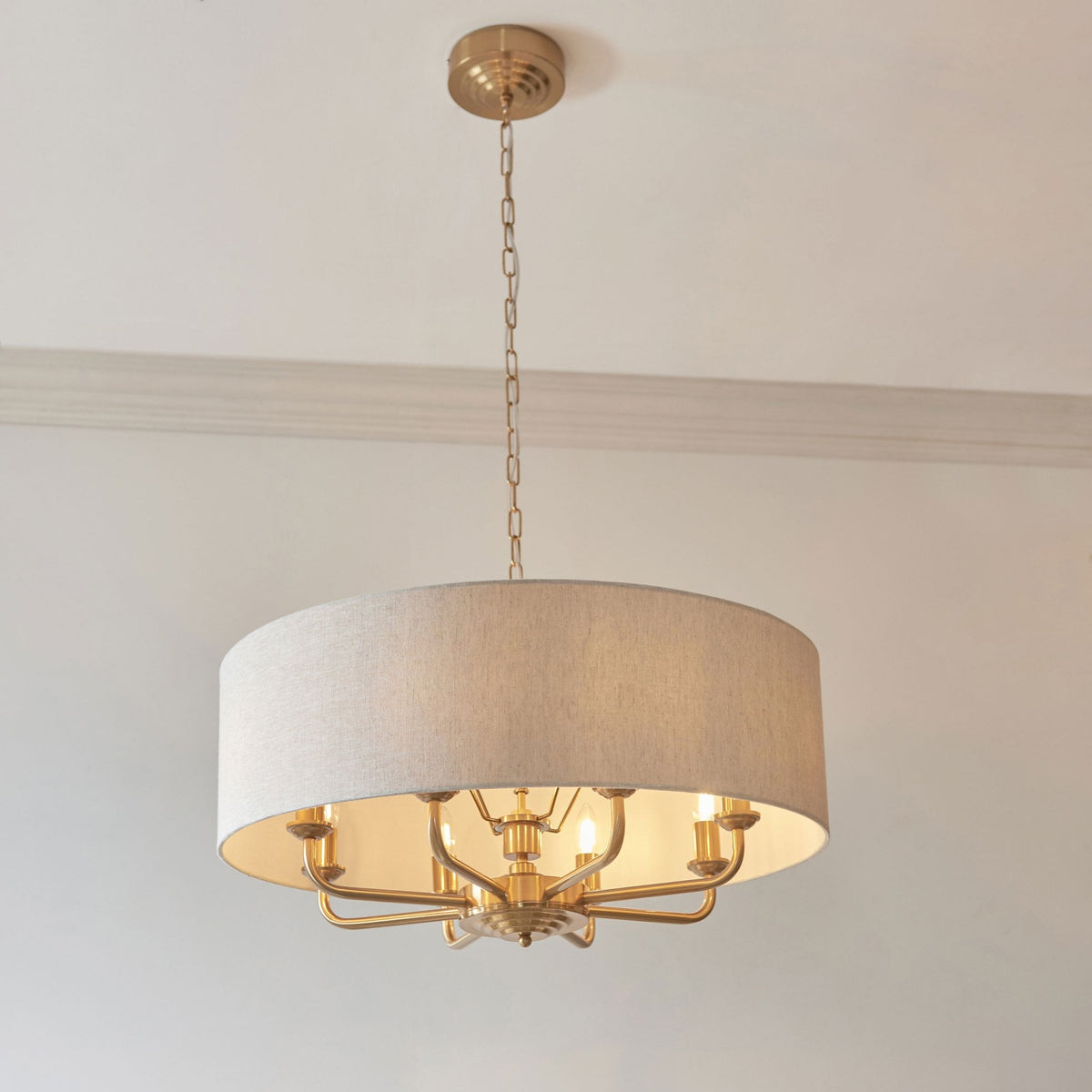 A gold chandelier with a light fabric drum shade hangs from a white ceiling.