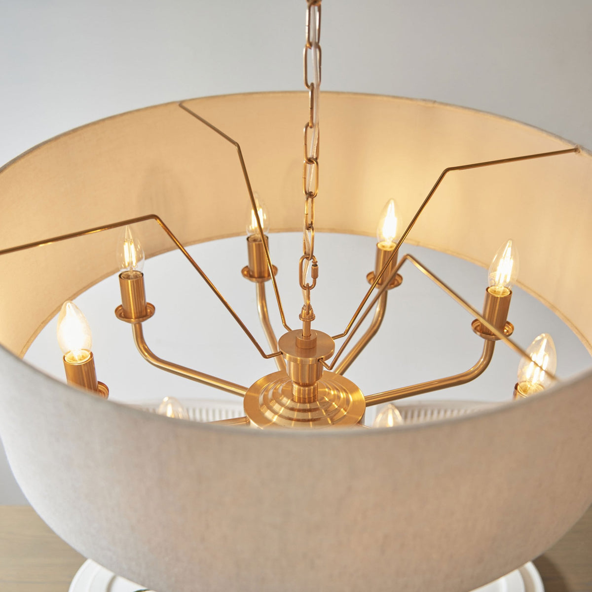 Close-up of the gold frame and exposed bulbs inside a light fabric drum shade.