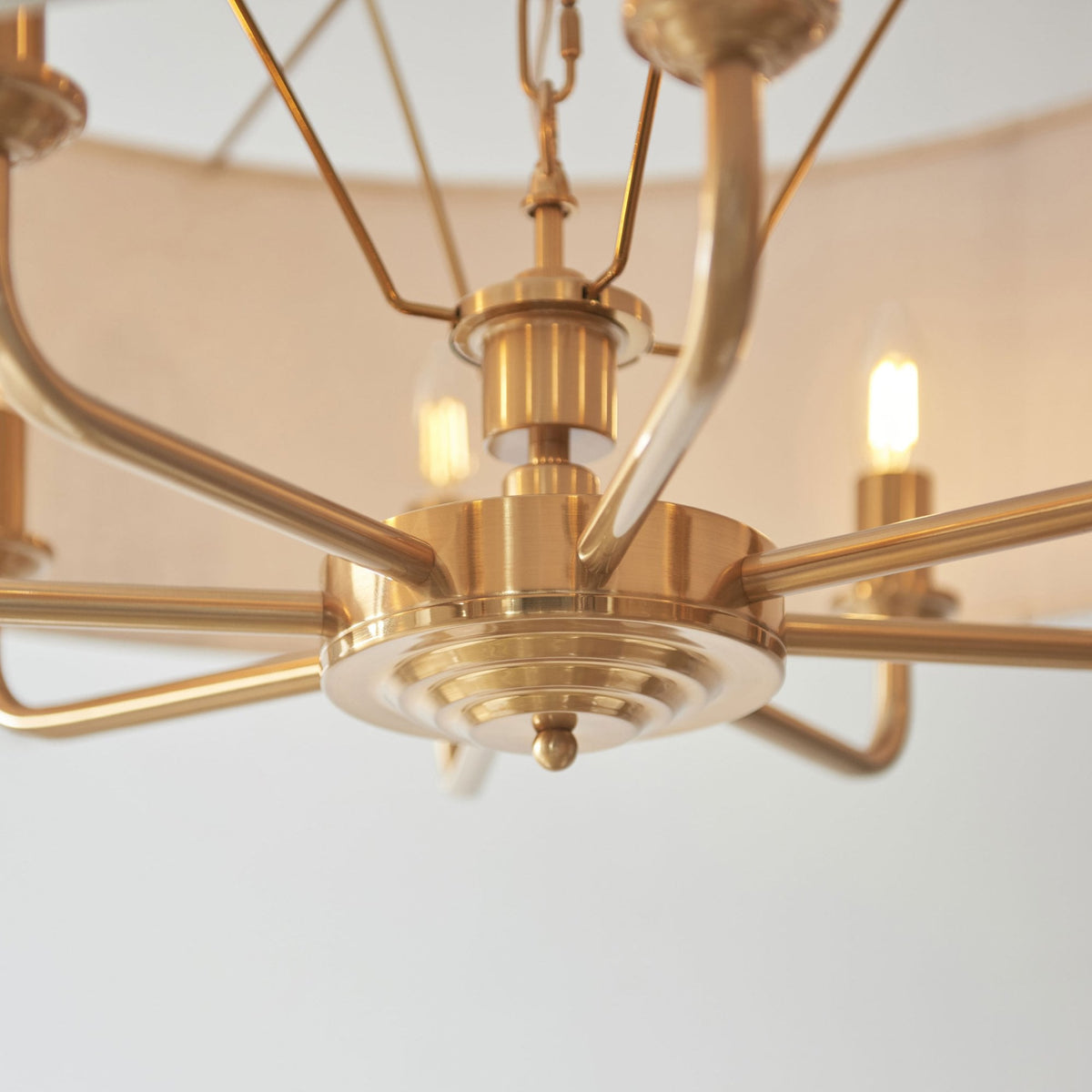 Close-up of the gold base and arms of a chandelier with exposed bulbs.