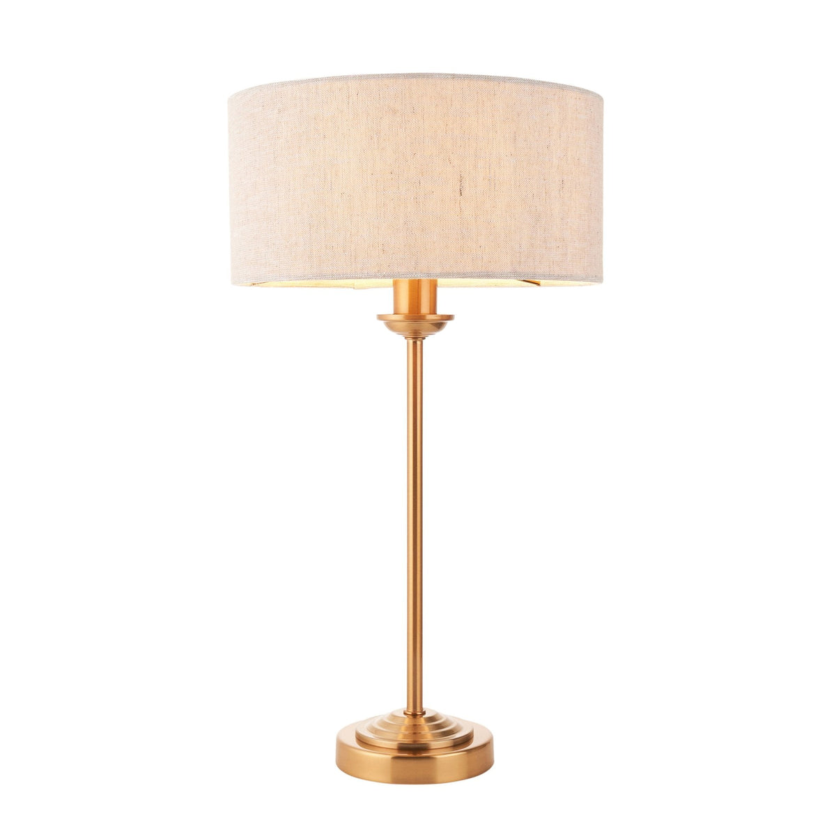A brass table lamp with a light linen drum shade on a white background.