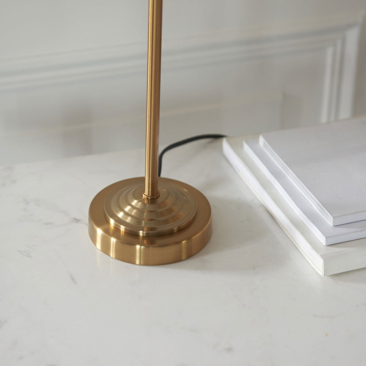Close-up of the round brass base of a table lamp on a white marble surface.