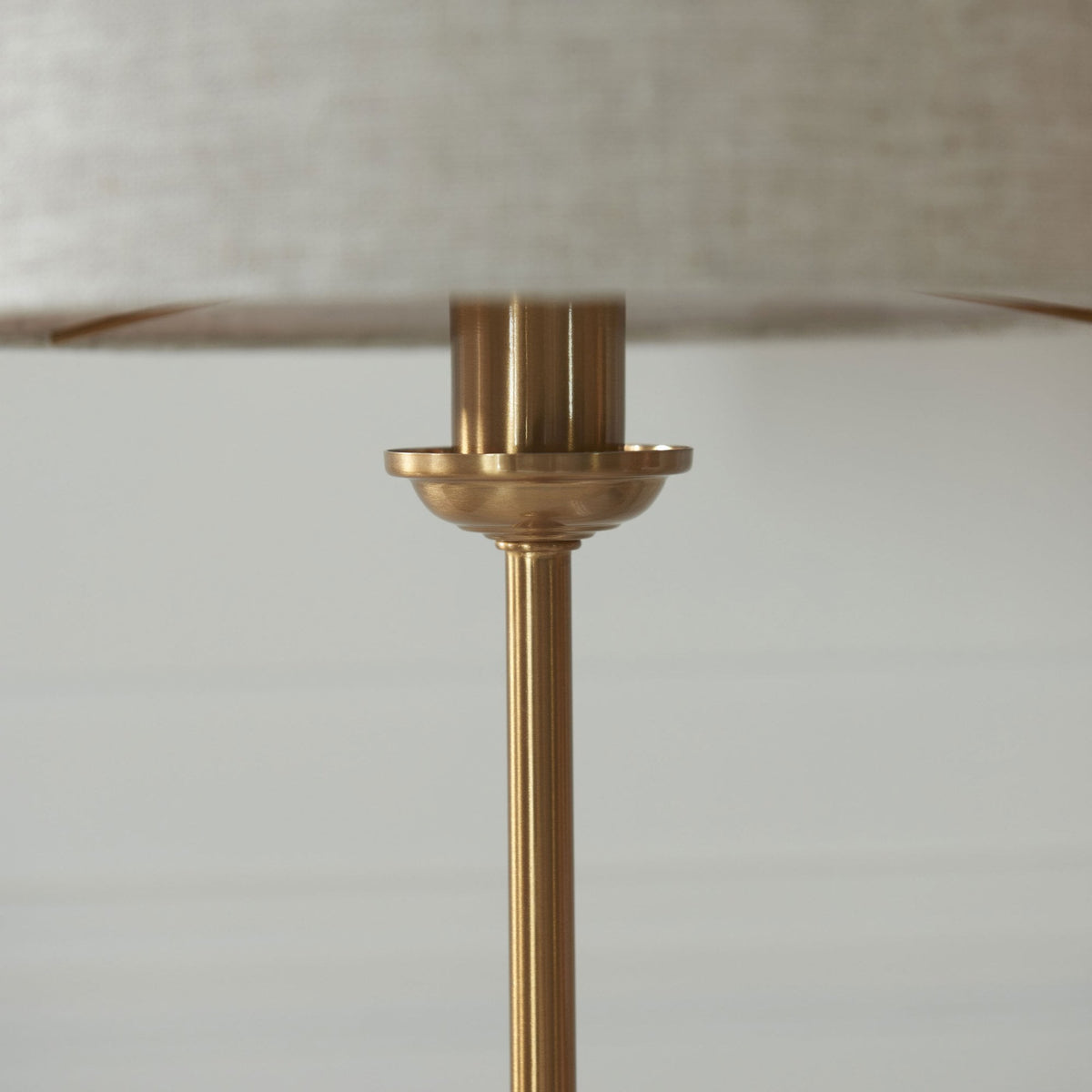 Close-up of the brass neck and base of a table lamp with a linen shade.