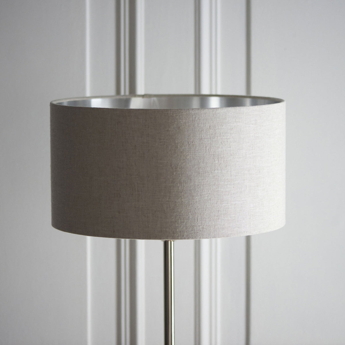 Close-up of a beige fabric lampshade with a silver interior, on a floor lamp.