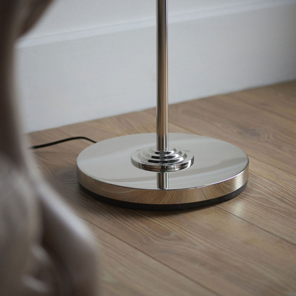The polished silver, round base of a floor lamp on a light wooden floor.