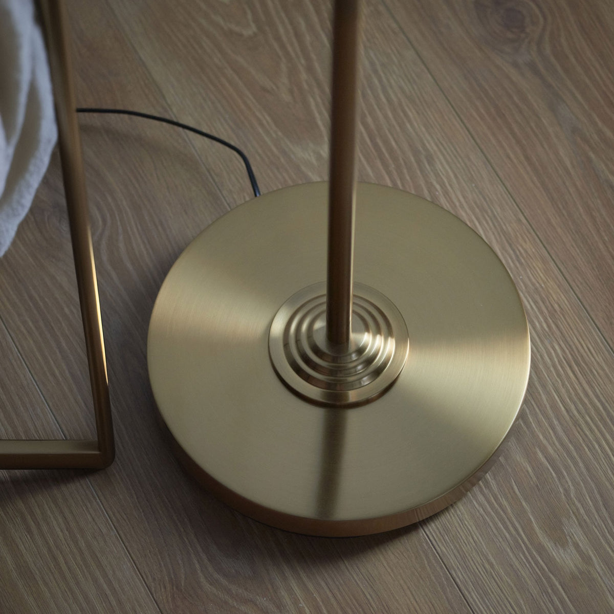 Close-up of the round, brushed brass base of a floor lamp on a light wooden floor.