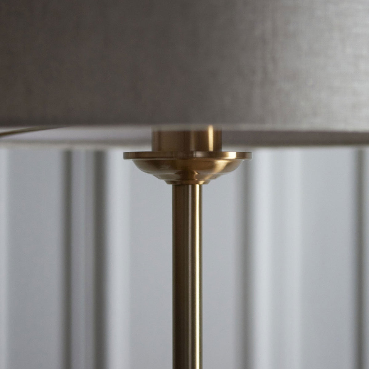 Detail of the brass neck connecting the light linen shade to the slender pole of a floor lamp.