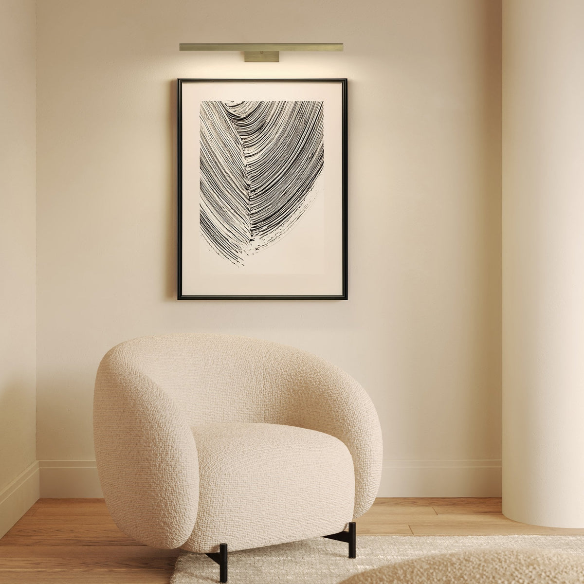 Cream boucle armchair with black legs, abstract art, and a picture light on a cream wall