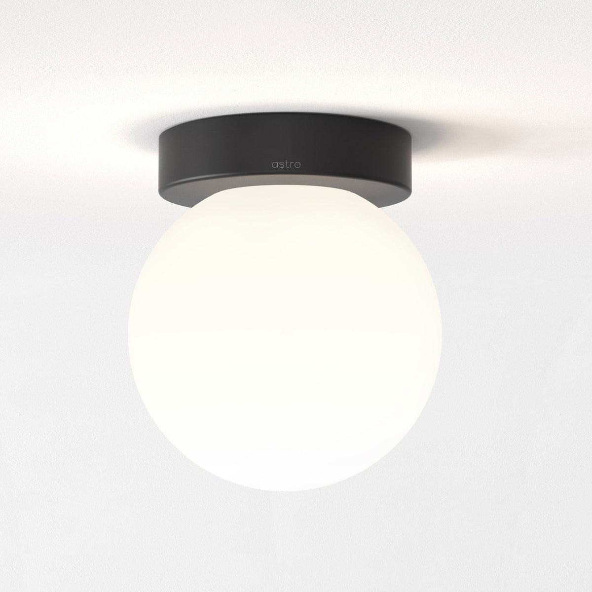 A minimalist white spherical light with a black base on a white ceiling.
