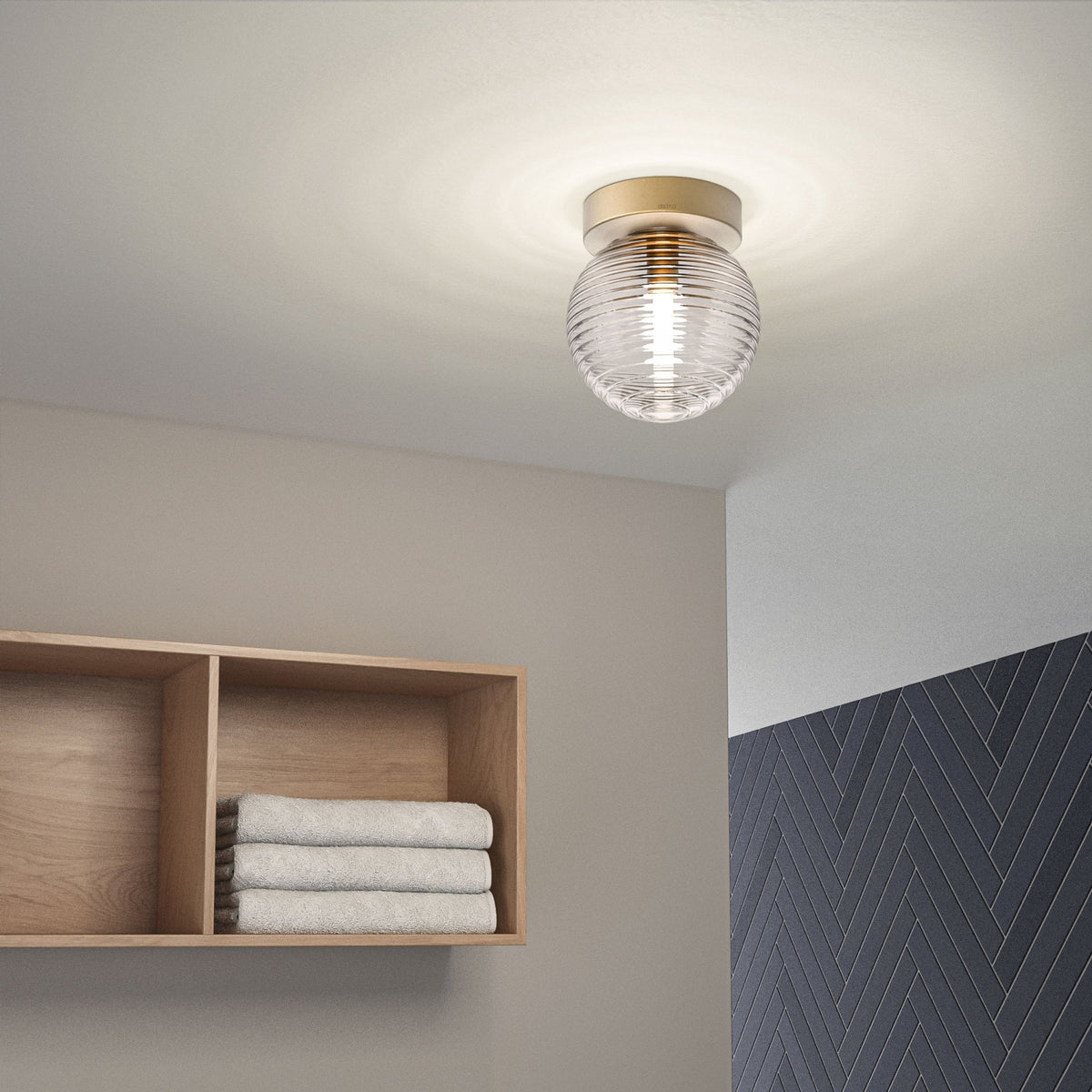 A round, clear glass ceiling light with horizontal ridges and a brass base illuminates a room