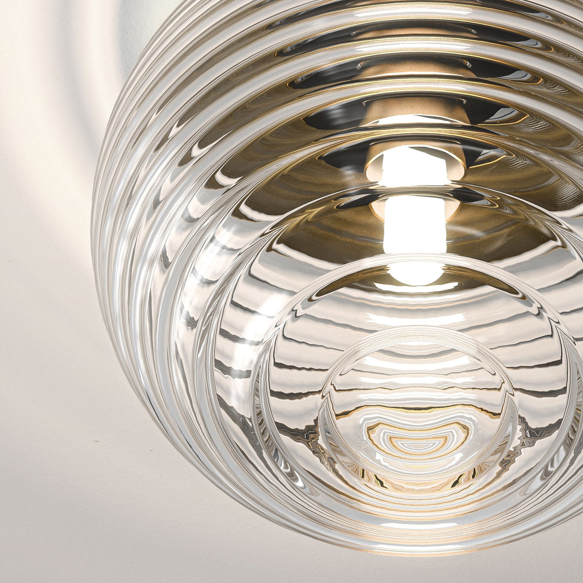 Close up of a clear glass pendant light with concentric ridges and a glowing bulb inside