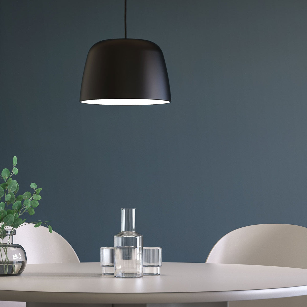 Black pendant light over a white round table with a glass vase of eucalyptus and two ribbed glass sets