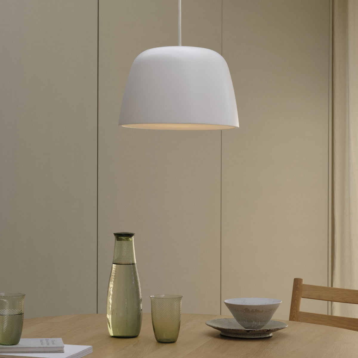 White pendant light hanging over a wooden table with a glass carafe, two glasses, and a bowl