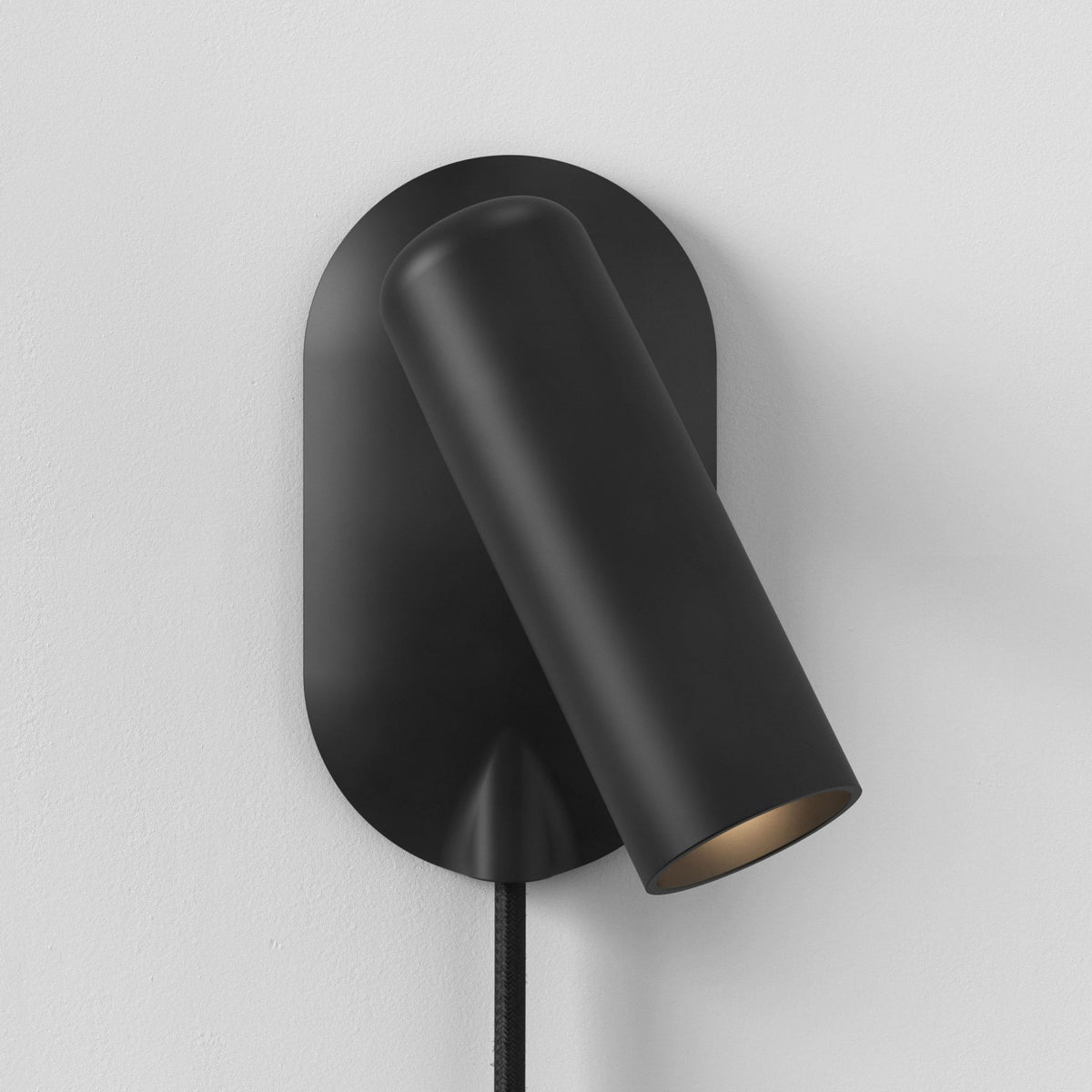 Black wall-mounted light fixture with an oval base and a cylindrical shade angled downwards