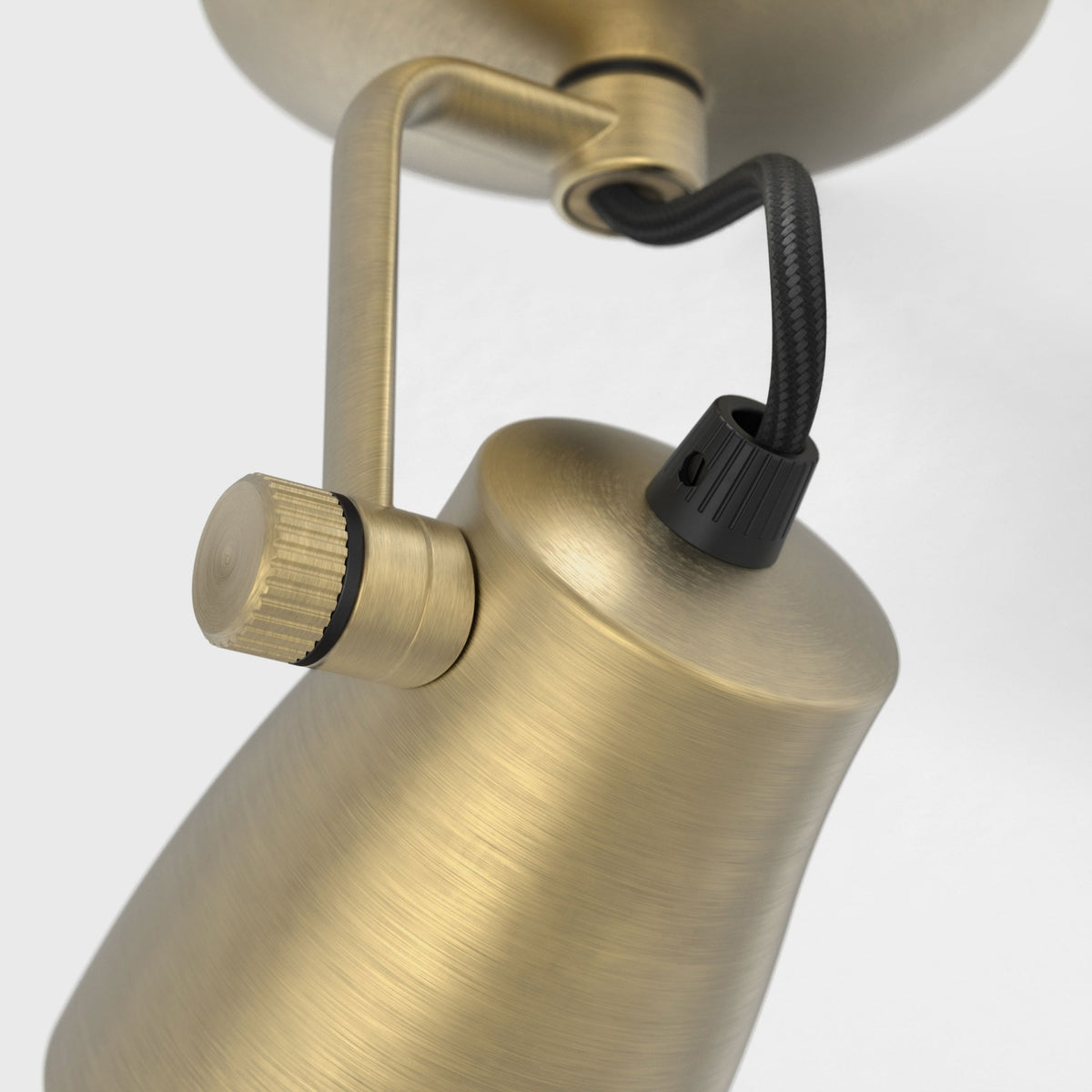Close-up of a brass ceiling spotlight with a black braided cable