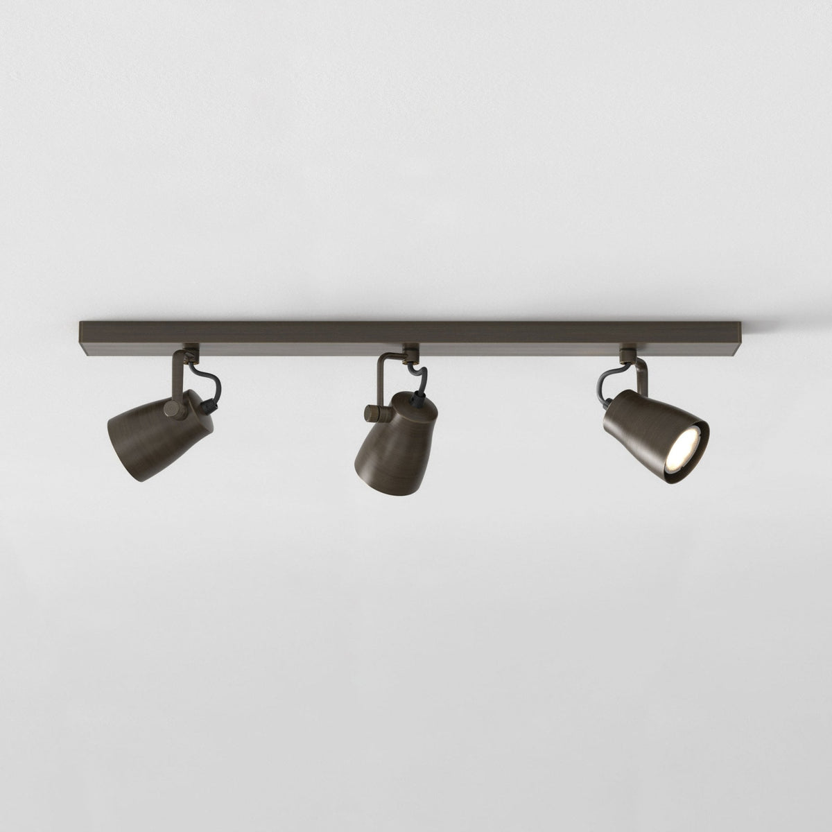 Three bronze track lights on a white ceiling, one light is illuminated