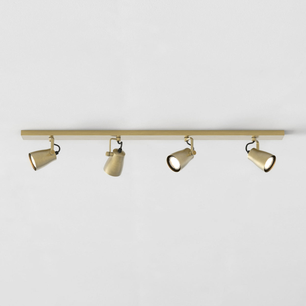 Four brass track lights on a brass bar against a white ceiling