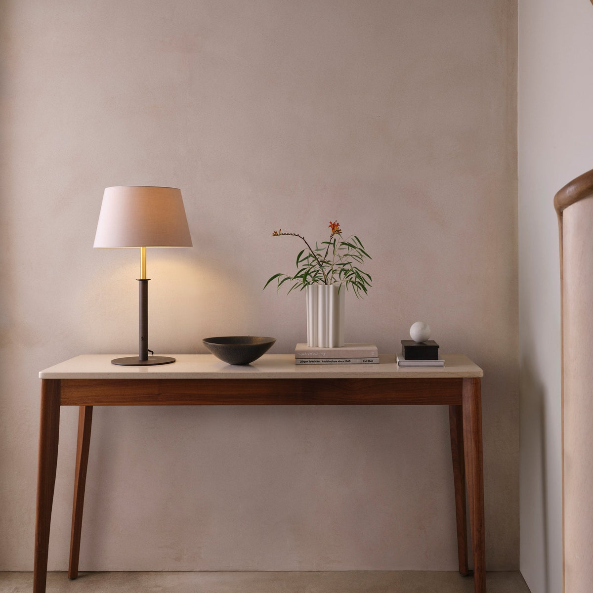 Console table with a lamp, a vase with flowers, a bowl, and books
