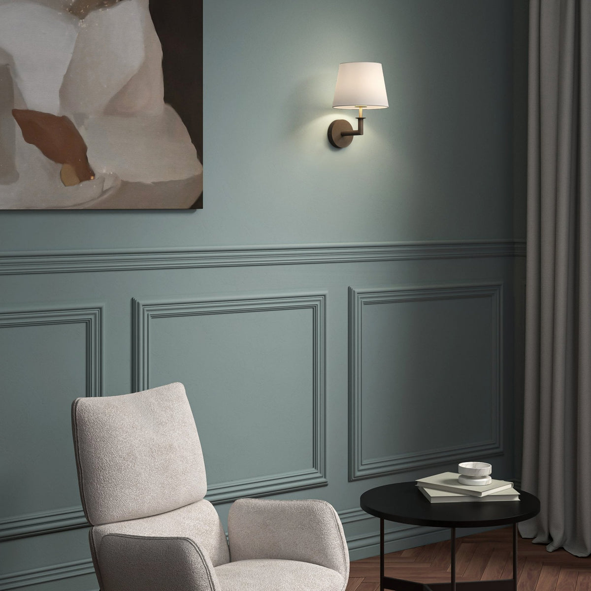 A light grey armchair, black side table with books and bowl, and a wall sconce on a teal paneled wall