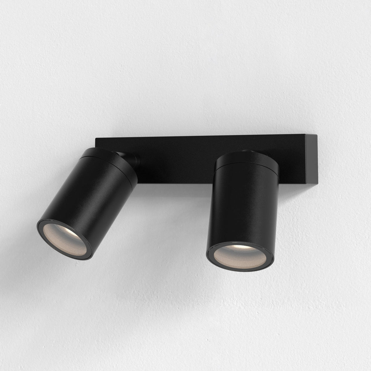 Two black cylindrical spotlights on a black rectangular base, mounted on a white wall