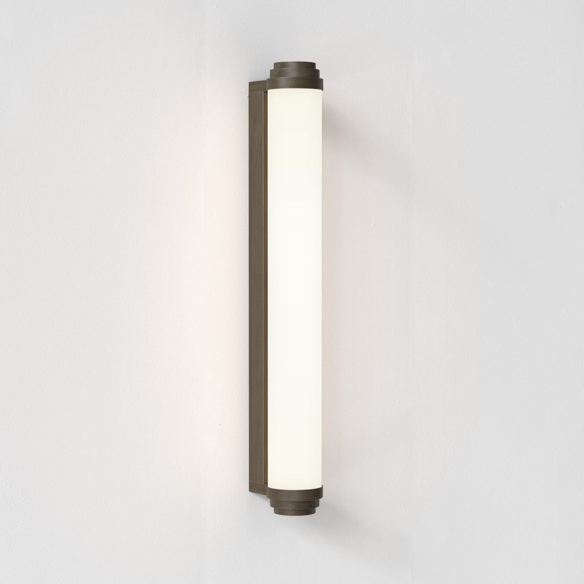 Vertical wall sconce with a dark bronze base and a long, cylindrical white glass shade