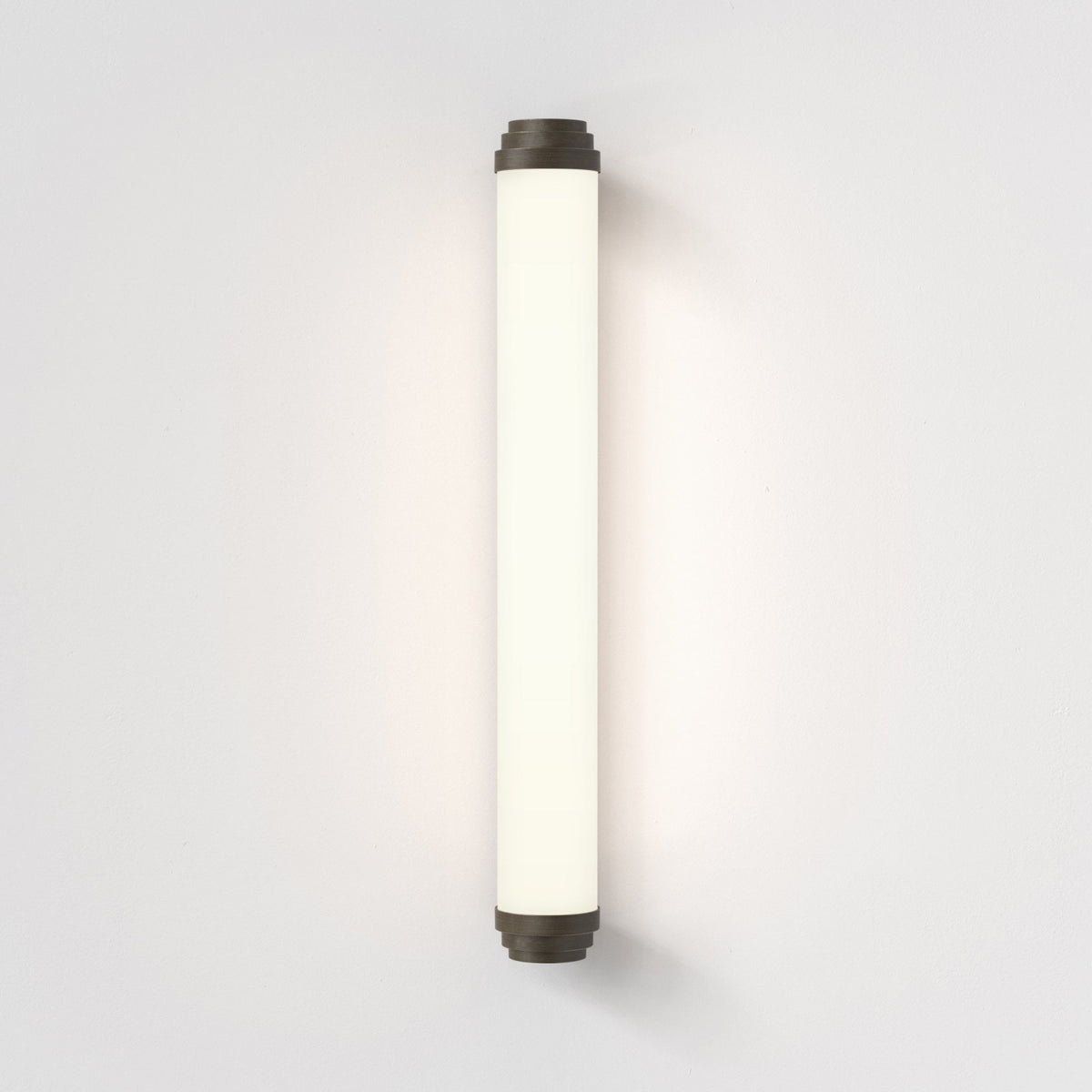 Vertical cylindrical wall light with dark bronze end caps and an illuminated white diffuser