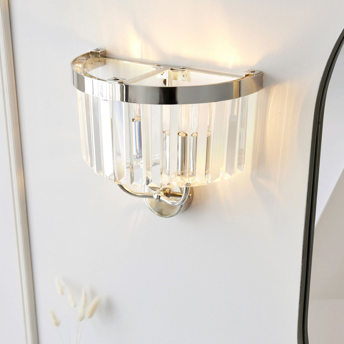 A chrome wall sconce with clear glass rods providing elegant up and down lighting on a white wall.