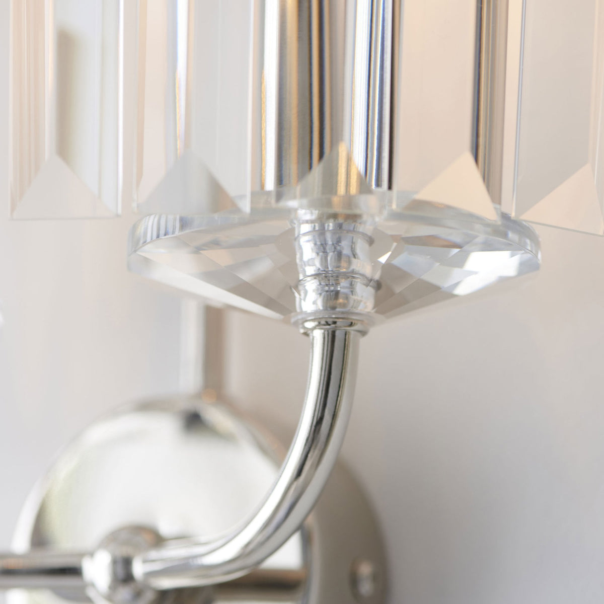 A close-up of the polished chrome arm and clear faceted glass detail of a modern wall sconce.