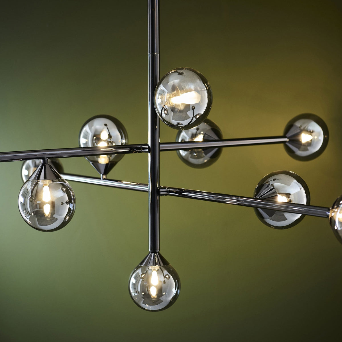 Close-up of a modern chrome chandelier, showing multiple spherical and teardrop-shaped smoked glass shades with glowing bulbs.