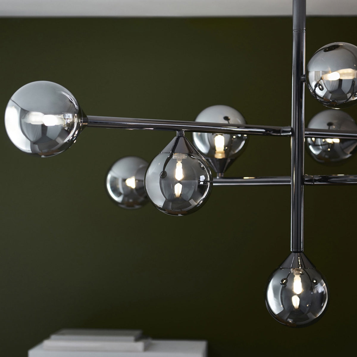 Detailed view of the chrome arms and smoked glass sphere and teardrop shades of a modern chandelier.